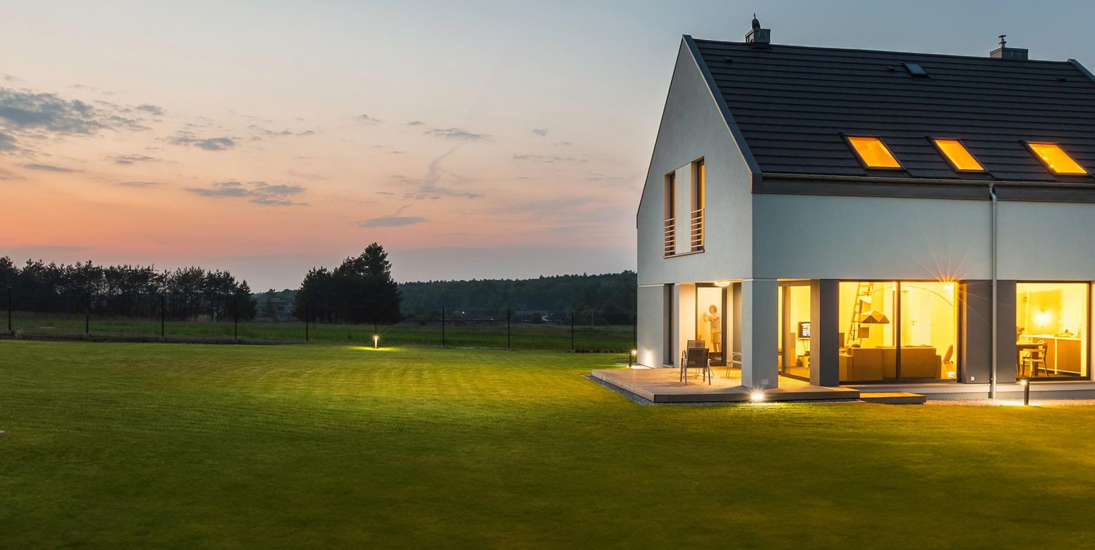 White house on a field at dusk with its lights on